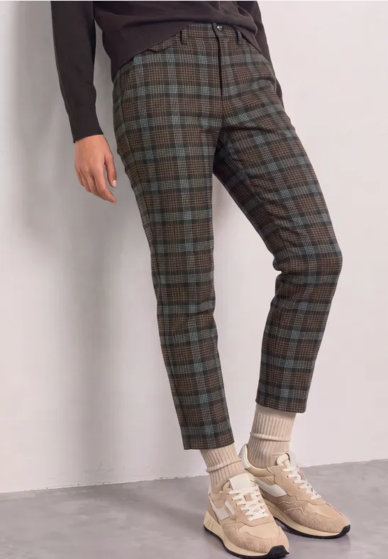 Persoon draagt groen-blauwe geruite broek met omgeslagen pijpen, beige sneakers en sokken.