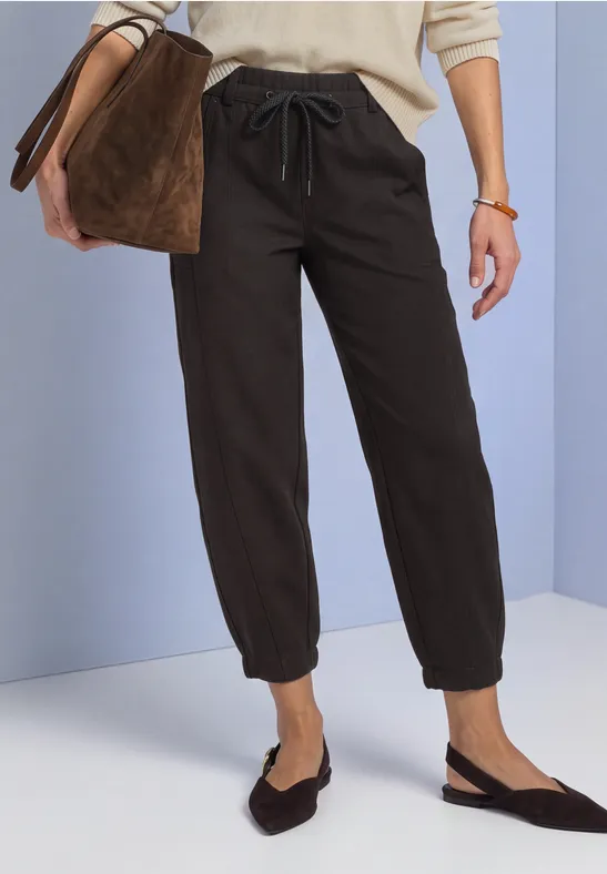 Schwarze Jogginghose mit Tunnelzug und Gummibündchen, kombiniert mit flachen Slingback-Schuhen und einer Tasche.