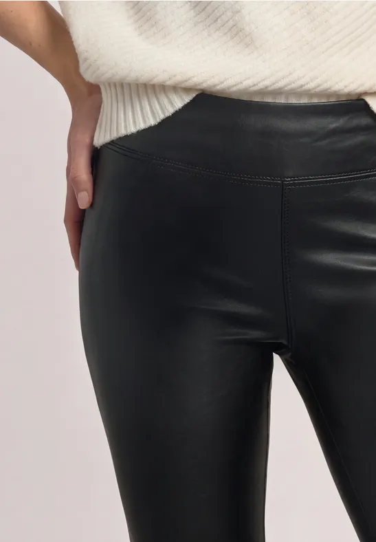 Frau trägt enge schwarze Lederleggings und weißen Strickpullover, Hand in der Hüfte.