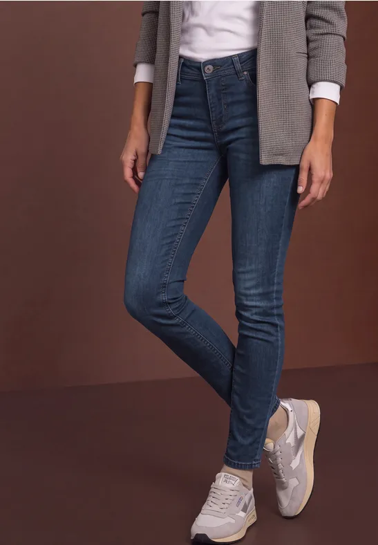 Femme en jeans skinny bleu, baskets blanches, chemise blanche et veste grise