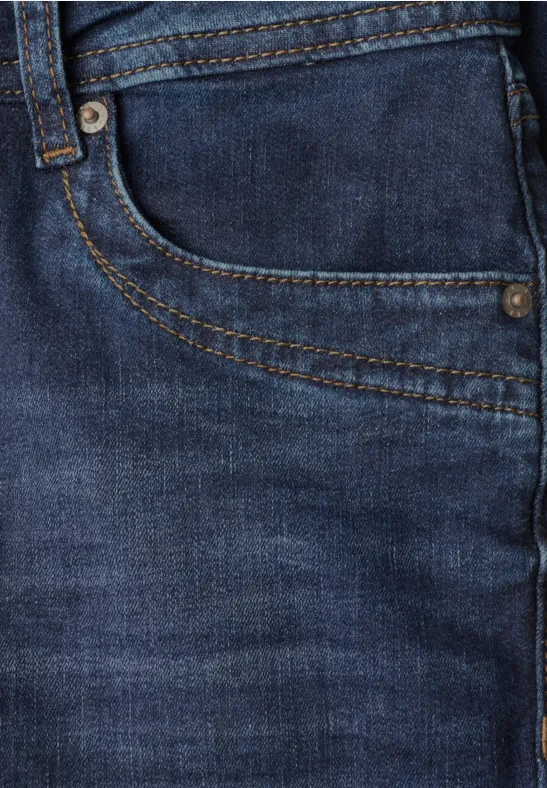 Gros plan d'un jean bleu montrant une poche, des coutures et des rivets métalliques.