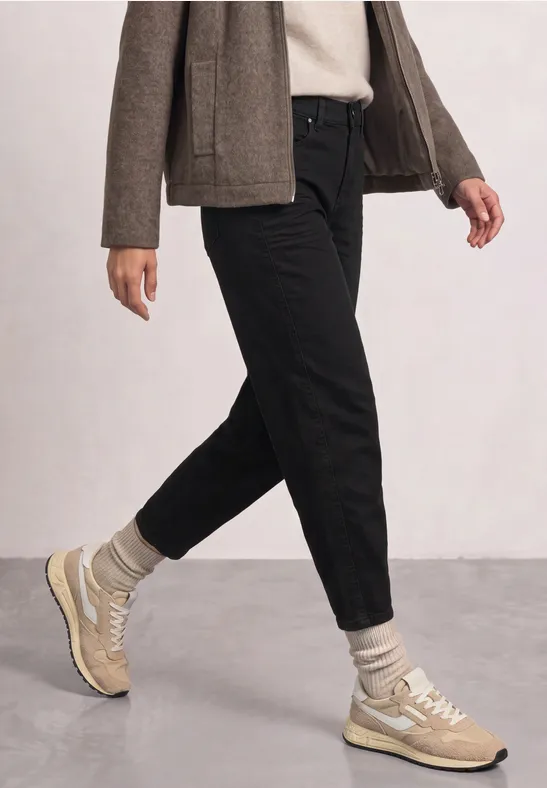 Une personne en pantalon noir, chaussettes grises et baskets beiges marchant.