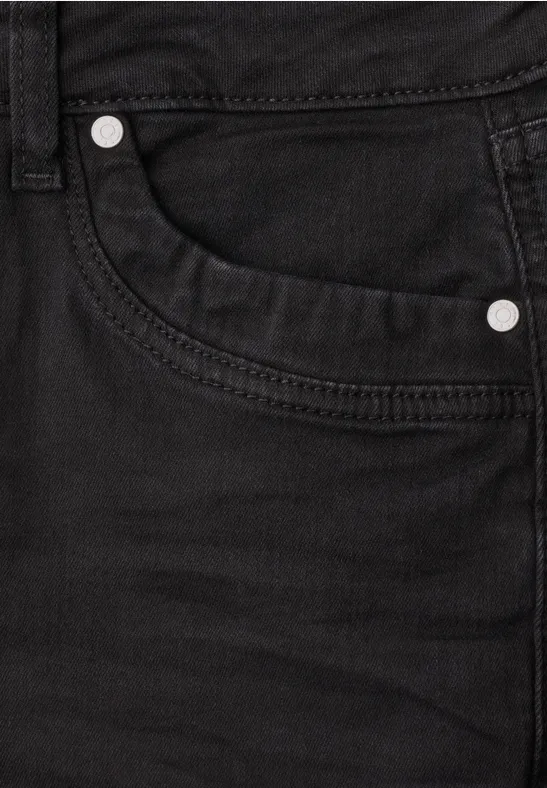 Gros plan sur un jean noir montrant une poche et des rivets métalliques.