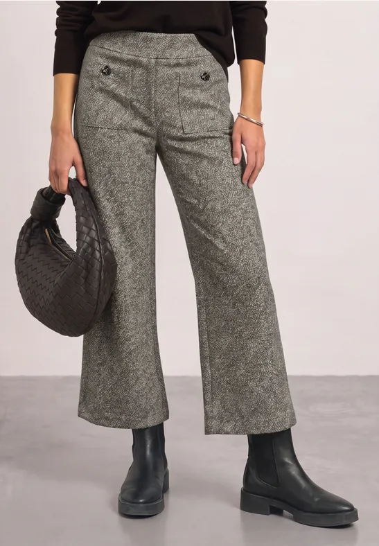 Pantalon gris évasé à boutons, sac noir tressé à la main et bottines noires.