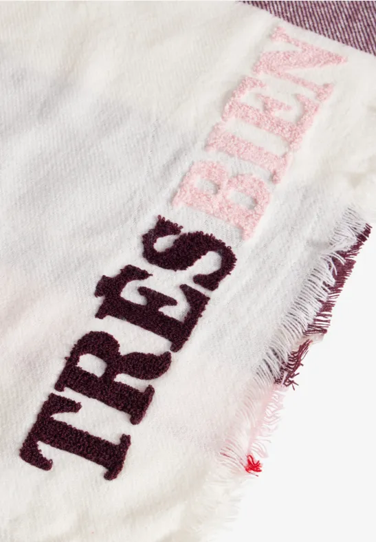 Weißer Schal mit Fransen und aufgesticktem Schriftzug 'TRÈS BIEN' in Rosa und Dunkelrot.