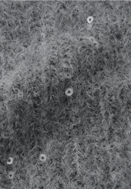 Nahaufnahme von flauschigem, grau gestricktem Stoff mit kleinen Pailletten.