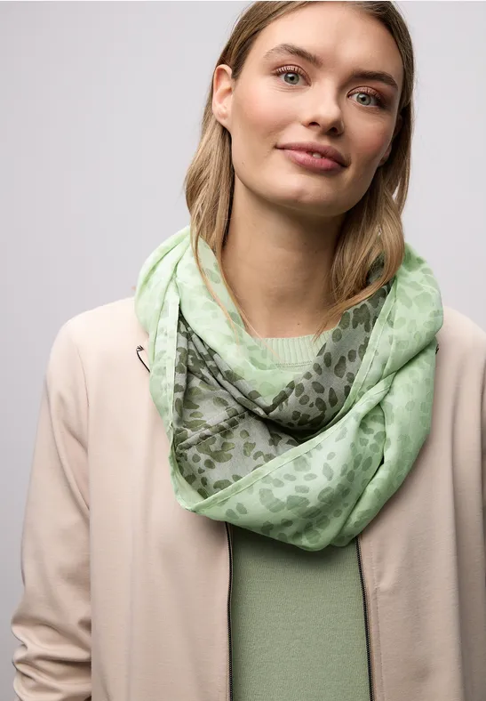 Une personne porte une veste beige, un t-shirt vert clair et une écharpe menthe à motifs.