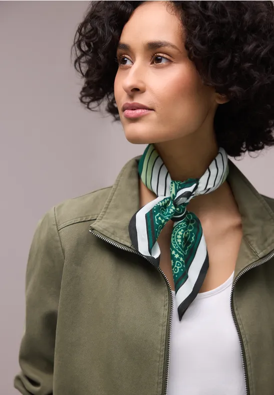 Personne aux cheveux bouclés porte un foulard rayé, un haut blanc et une veste kaki.