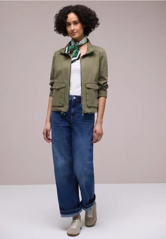 Personne porte veste verte, top blanc, jean ample, foulard et baskets.