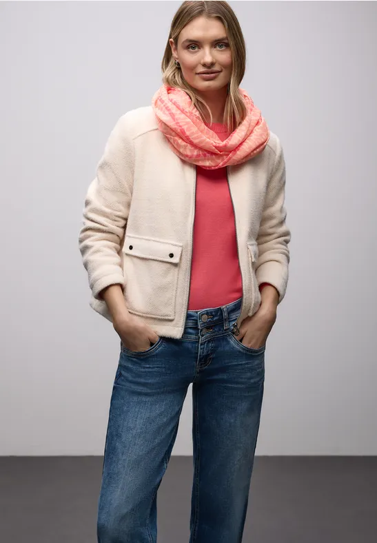 Person in heller Jacke, rotem Shirt, blauen Jeans und korallfarbenem Schal.