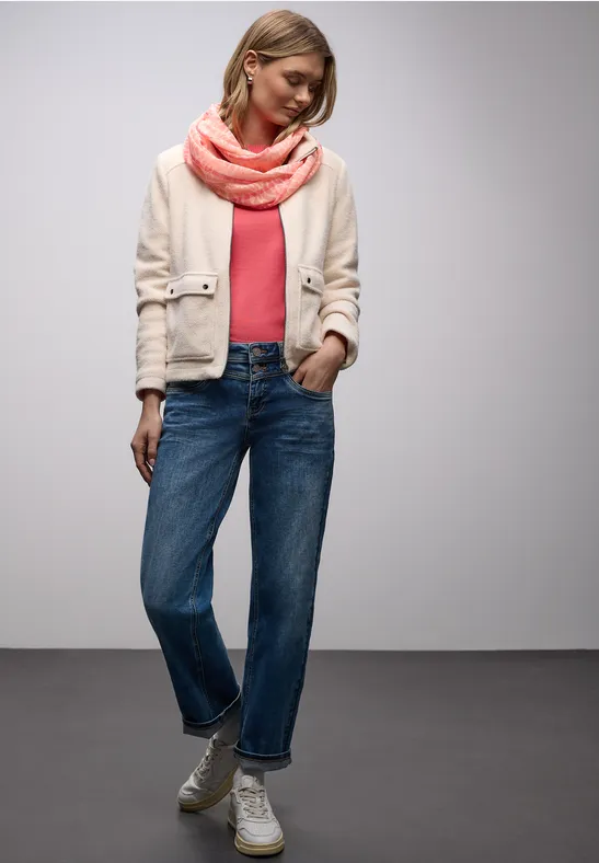 Eine Person in Jeans, Sneakers, rosa Oberteil, hellem Blazer und rosafarbenem Schal.