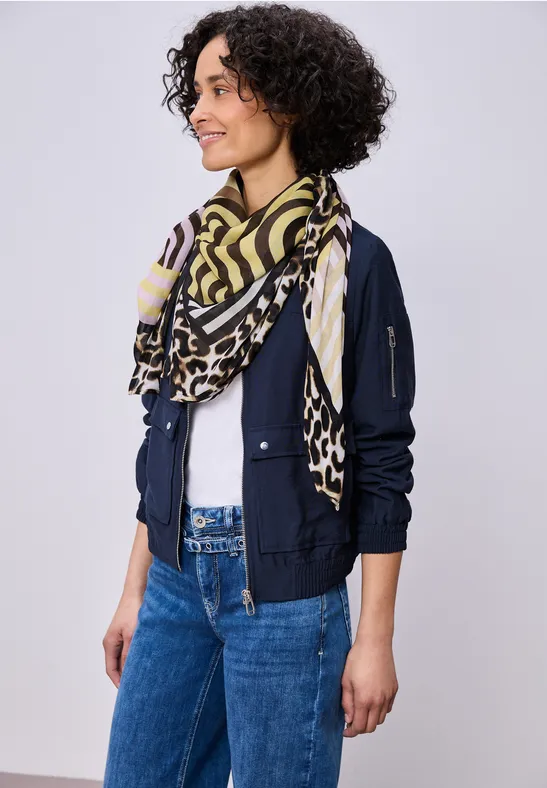 Persoon met wit T-shirt, donkerblauwe bomberjack, geel-zwart dessin sjaal en blauwe jeans.