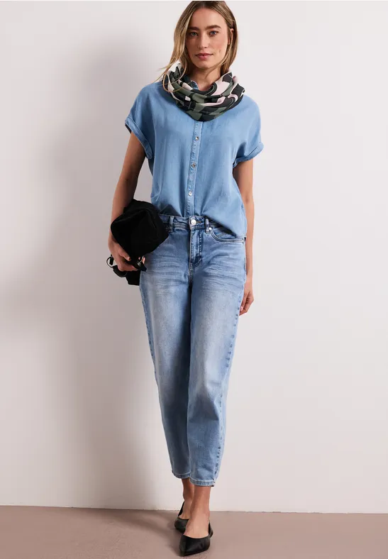 Vrouw in lichtblauw denimset met blauw topje, spijkerbroek, sjaal en zwarte hoed