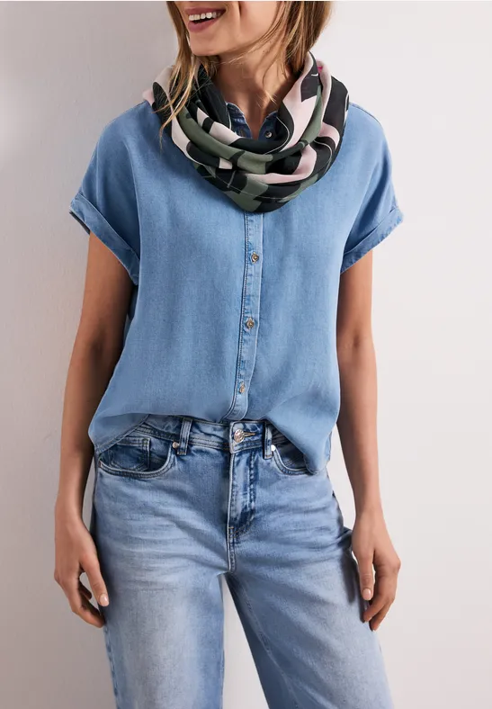 Een vrouw draagt een lichtblauw denim overhemd en jeans met een kleurrijke sjaal.