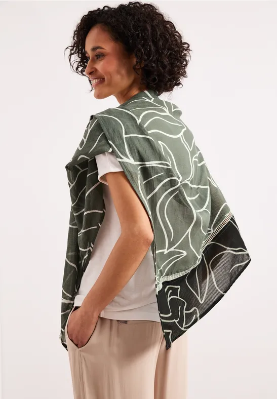 La personne vue de profil porte un châle vert à motif blanc sur les épaules et a les cheveux frisés.