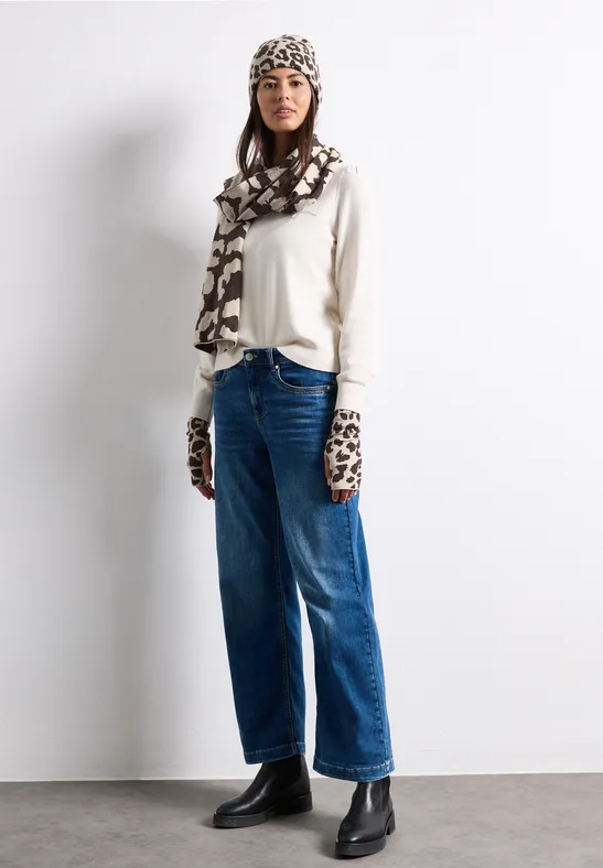 Femme en pull blanc, jean ample, bottines noires, bonnet, écharpe et moufles imprimées léopard.