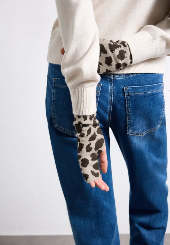 Personne en jean bleu et pull crème portant des mitaines imprimé léopard sur fond neutre.