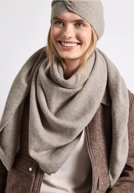 Glimlachende vrouw met taupekleurige sjaal en hoofdband voor een witte achtergrond.