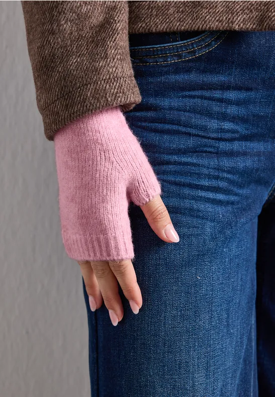 Nahaufnahme einer Person in blauen Jeans und braunem Pullover, die rosa fingerlose Handschuhe trägt.