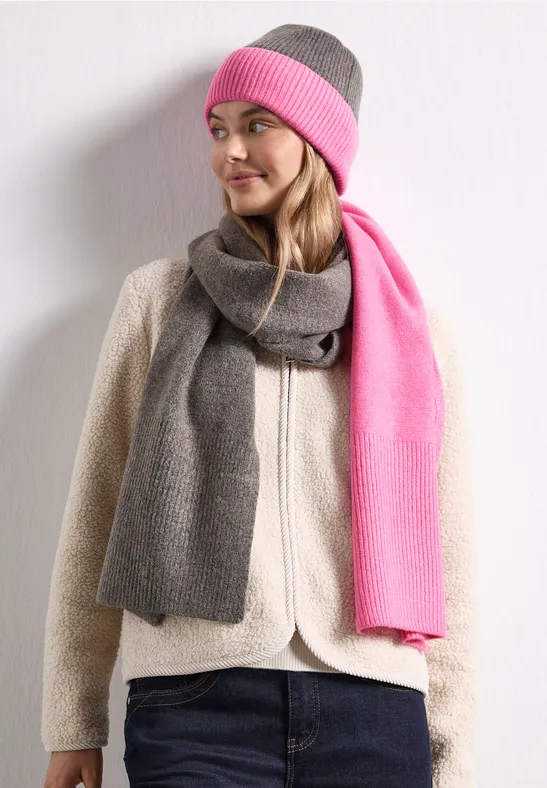 Vrouw met grijs-roze muts en sjaal, witte fleecejas, kijkt opzij.