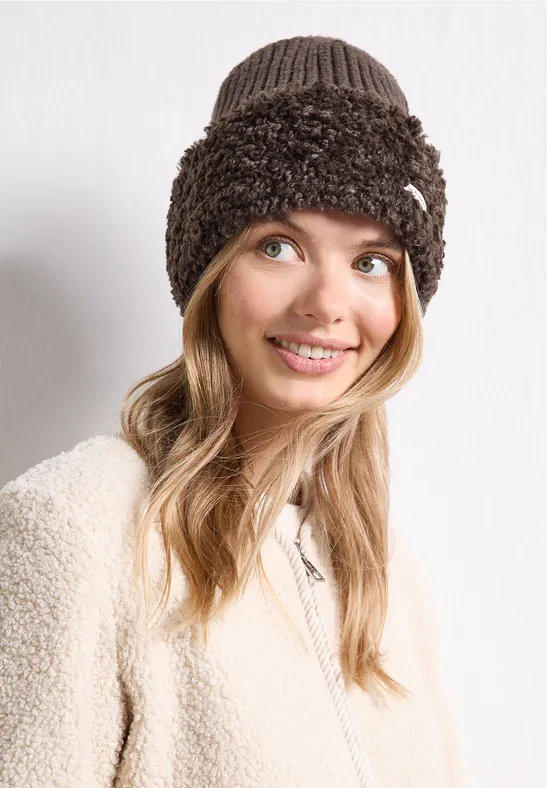 Jonge vrouw lacht, draagt een beige teddyjas en een bruine, pluche gebreide muts.