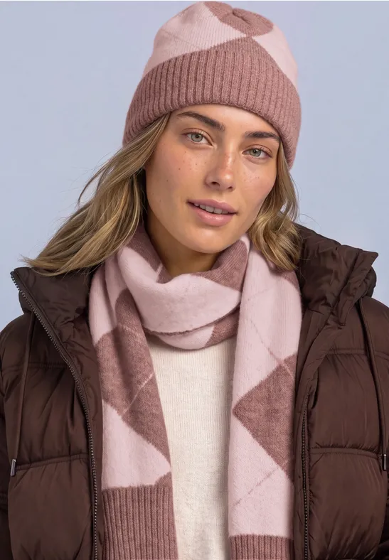 Frau mit rosa-beiger Strickmütze und Schal trägt braune Steppjacke vor hellem Hintergrund.