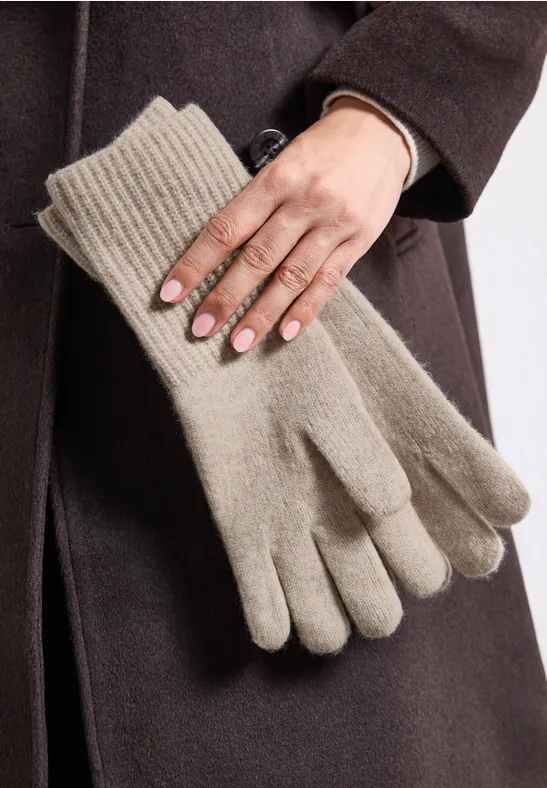 Een persoon houdt een paar beige gebreide handschoenen voor een donkere jas.