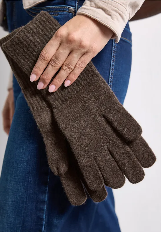 Braune, gestrickte Fünffinger-Handschuhe, in einer Hand gehalten, vor einer Jeanshose.