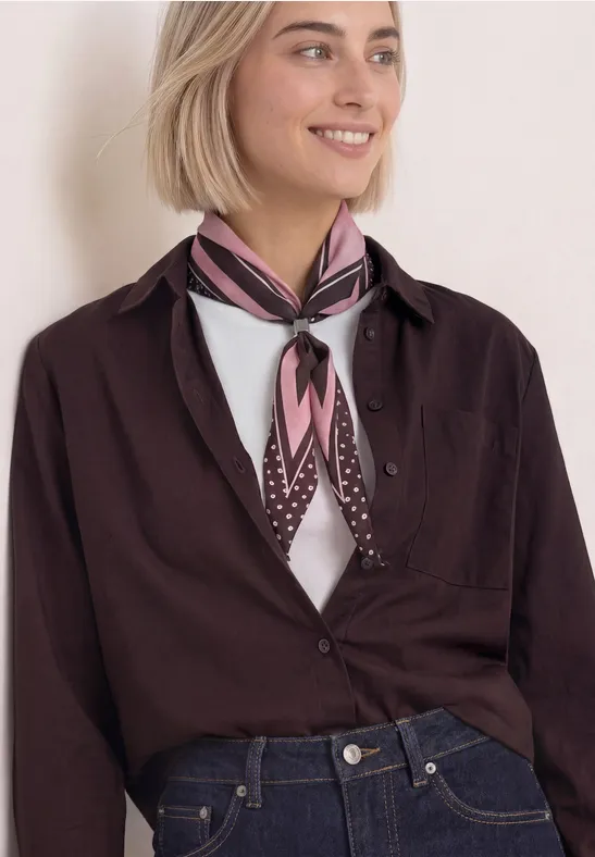 Lächelnde Frau in dunklem Hemd, Jeans und rosa-braunem Halstuch.