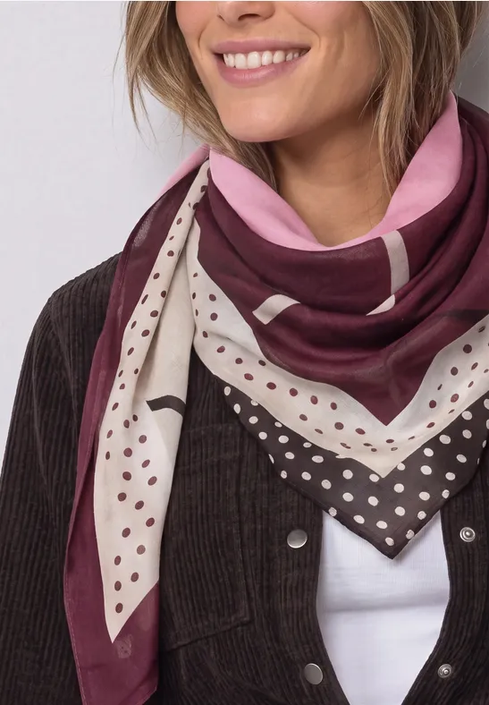 Frau mit lächelndem Gesicht, trägt ein pink-braunes Halstuch mit Punkten über weißem Top und Cordjacke.