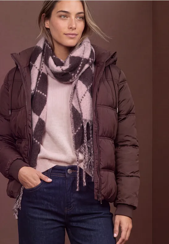 Femme en doudoune marron, pull beige, écharpe à motifs et jean sur fond marron.