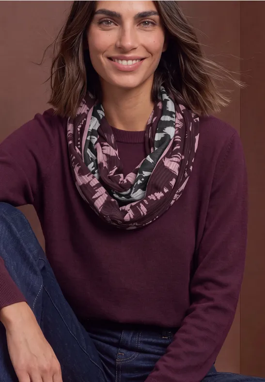 Femme souriante en pull bordeaux, écharpe imprimée en boucle et jean.