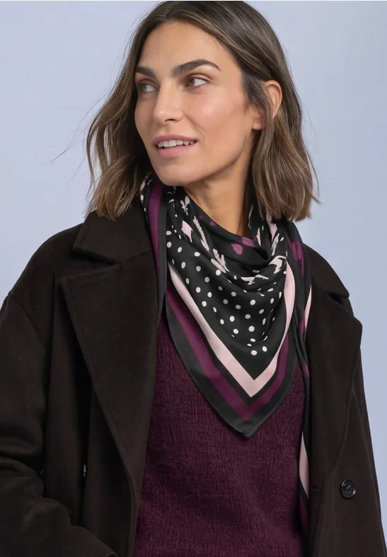 Frau mit schwarzem Mantel, bordeauxrotem Pullover und schwarz-weiß gepunktetem Halstuch mit rosafarbenen Streifen.