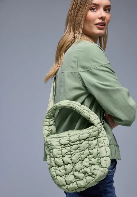 Frau trägt grünen Blazer, Jeans und eine gepolsterte, hellgrüne Handtasche im Arm.