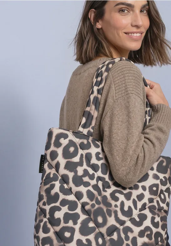 Vrouw in beige trui lacht en draagt een shopper met luipaardprint over haar schouder.