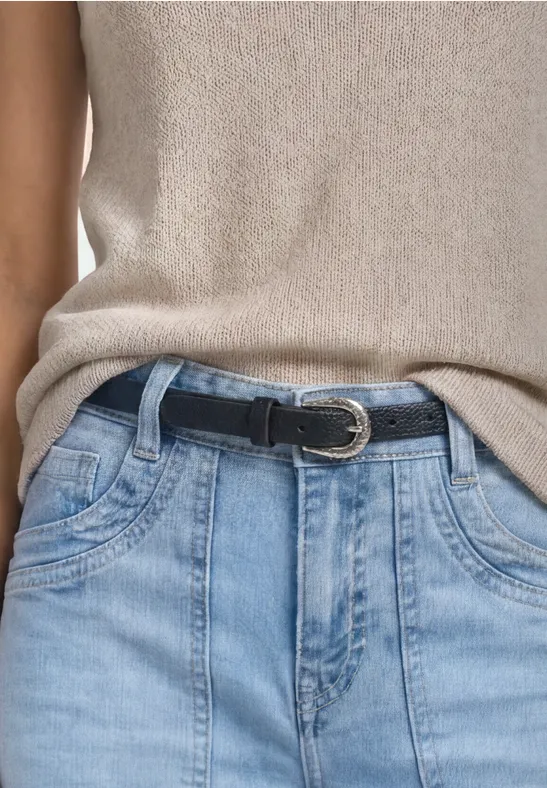 Eine Person trägt einen beigefarbenen Top, hellblaue Jeans und einen schwarzen Gürtel.