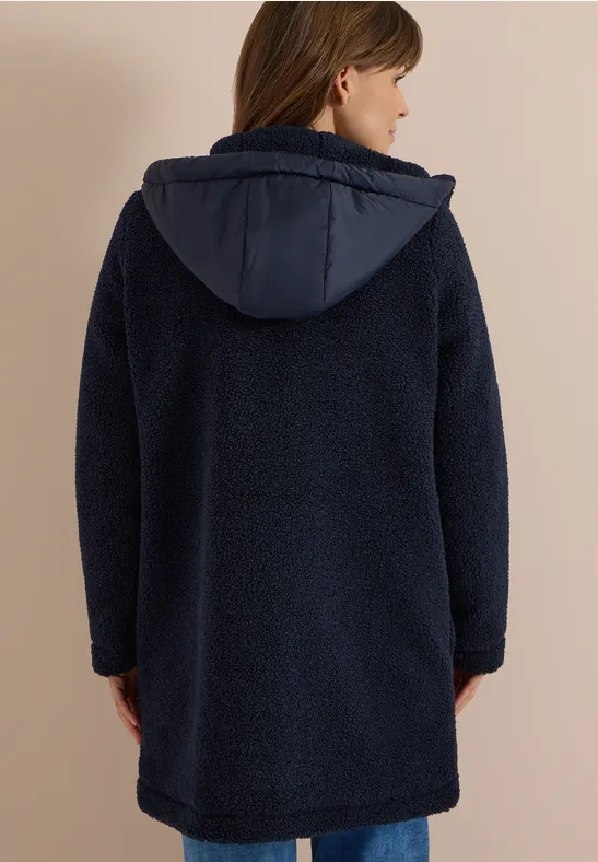 Frau von hinten in einem dunkelblauen, knielangen Teddy-Fleece-Mantel mit Kapuze.