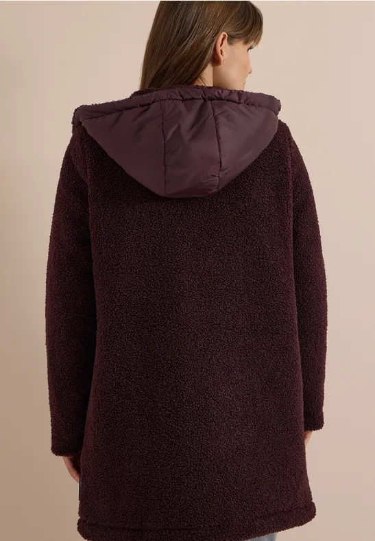 Eine Person von hinten in einem dunkelvioletten, flauschigen Teddy-Kapuzenmantel.