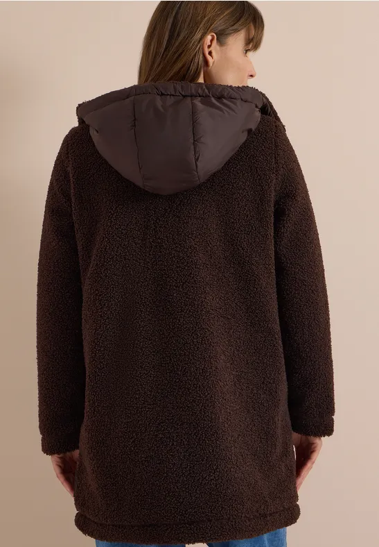 Rückansicht einer Person in einem braunen, langen Teddyplüsch-Mantel mit Kapuze.