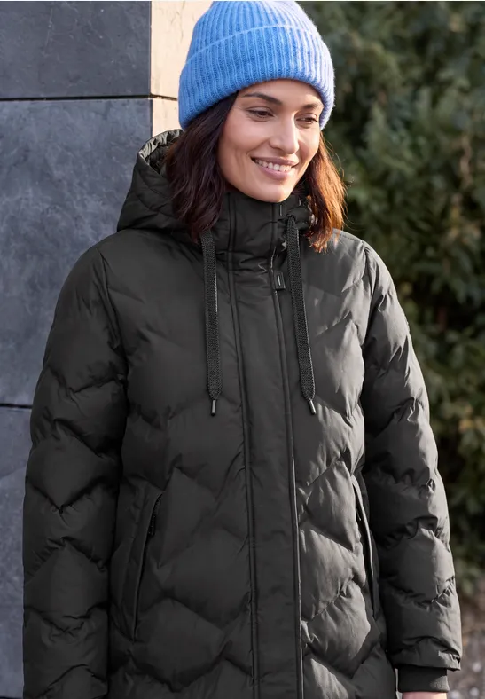 Femme souriante en manteau matelassé noir et bonnet bleu clair à l'extérieur.