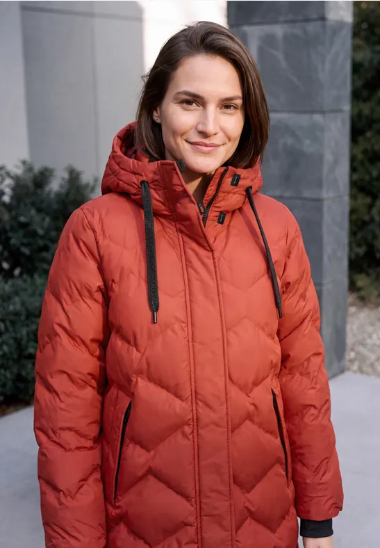 Une femme en doudoune rouge sourit en extérieur.