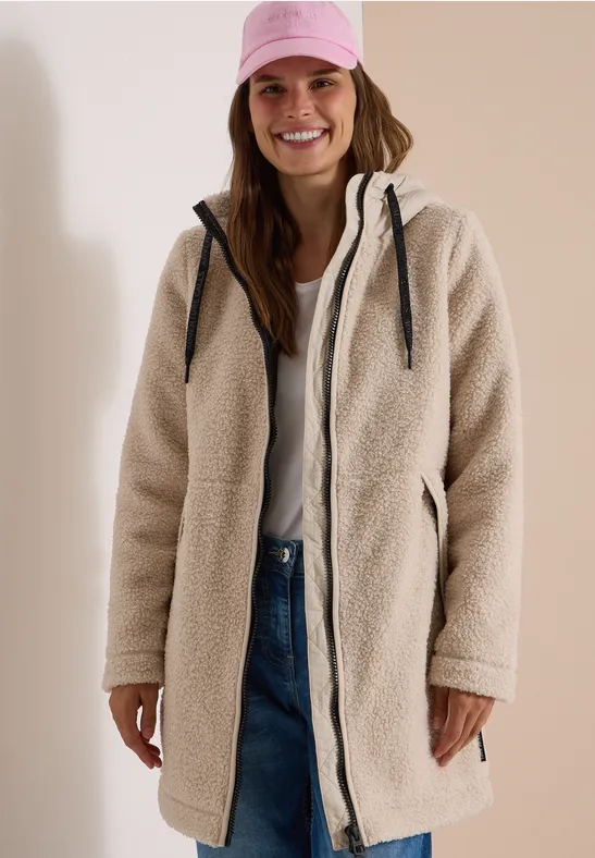 Vrouw lachend in beige teddyjas en roze pet.