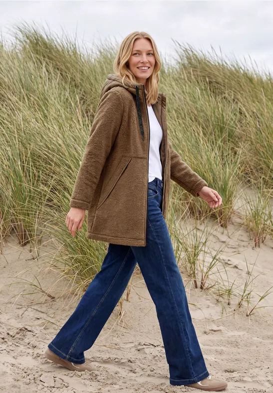 Eine Frau spaziert fröhlich am Strand vor Sanddünen.