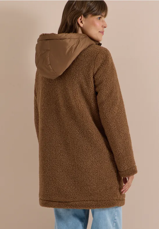 Een vrouw van achteren draagt een bruine teddyjas met capuchon, zacht en warm.