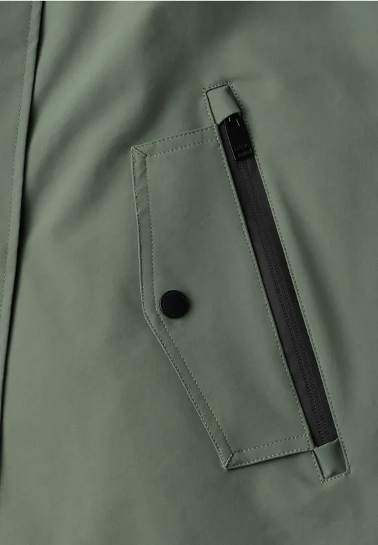 Close-up einer grünen Jackentasche mit schwarzem Reißverschluss und Druckknopf.