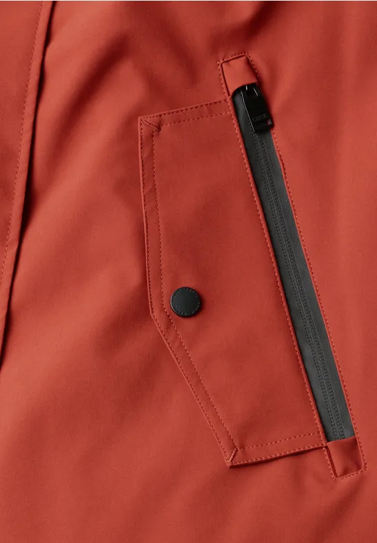 Nahaufnahme einer rostroten Jacke mit schrägem schwarzen Reißverschluss und Druckknopf an der Tasche.