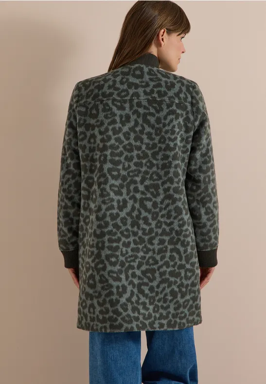 Frau steht mit dem Rücken zur Kamera und trägt einen knielangen, grünen Leopardenmantel zu Jeans.