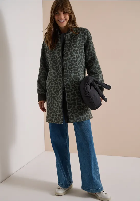 Frau in grün-grauem Leo-Mantel, weiten Jeans und Sneakers, hält eine schwarze Tasche.