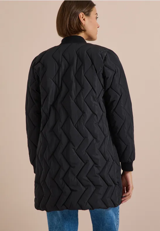 Femme de dos portant un manteau matelassé long noir à motif zigzag.