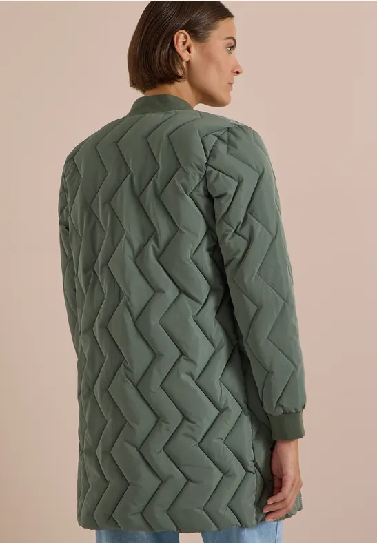 Une femme porte un manteau matelassé olive long avec motif zigzag, vue de dos.